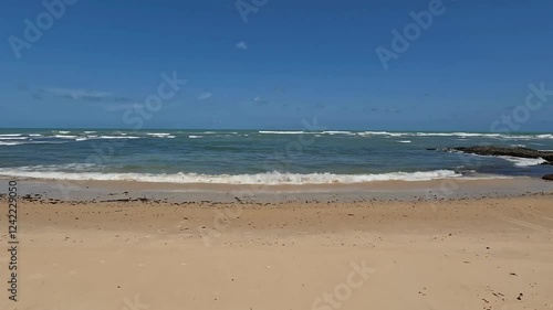 Waves of a calm sea reaching the sandy shore on a sunny day.