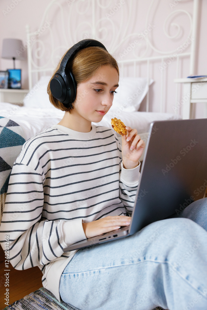 Teenage girl eating cookie and watching laptop during doing homework Teenage girl eating cookie and watching laptop during doing homework