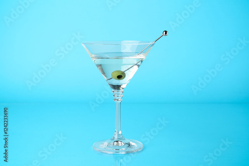 Martini cocktail with olive in glass on light blue background