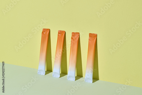 Three vibrant orange citrus stick packs are displayed against a yellow