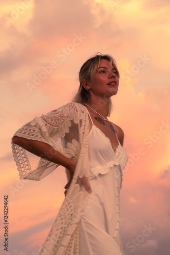 Woman in white dress poses against a vibrant sunset sky