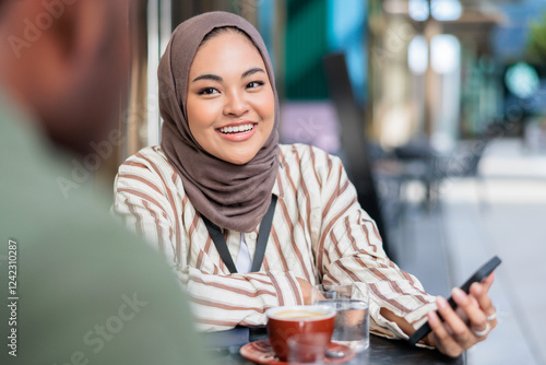 Smiling muslim woman talking with colleague while having coffee photo