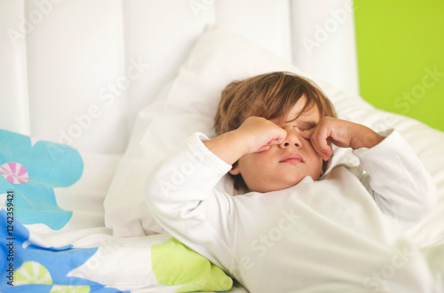 Small child waking up in a cozy bed on a bright morning photo