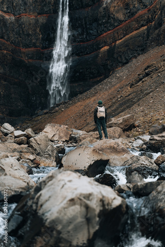 Male Hiker From Behind Standing On Stones By Waterfall photo