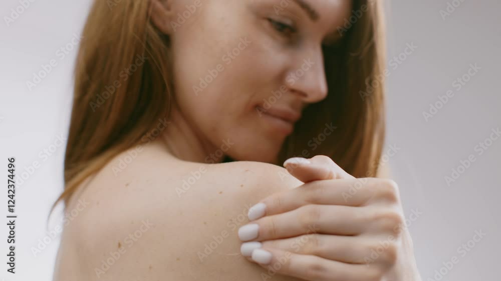 A young lady with long hair is applying skin care product on her shoulder in a calm, isolated environment. The focus is on her gentle movements and the creamy texture of the product. A young lady with long hair is applying skin care product on her shoulder in a calm, isolated environment. The focus is on her gentle movements and the creamy texture of the product.