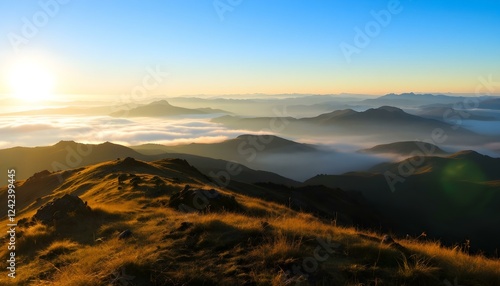 Sunrise over misty mountain range with golden grassy slopes, blue sky, and distant peaks fading into the horizon.