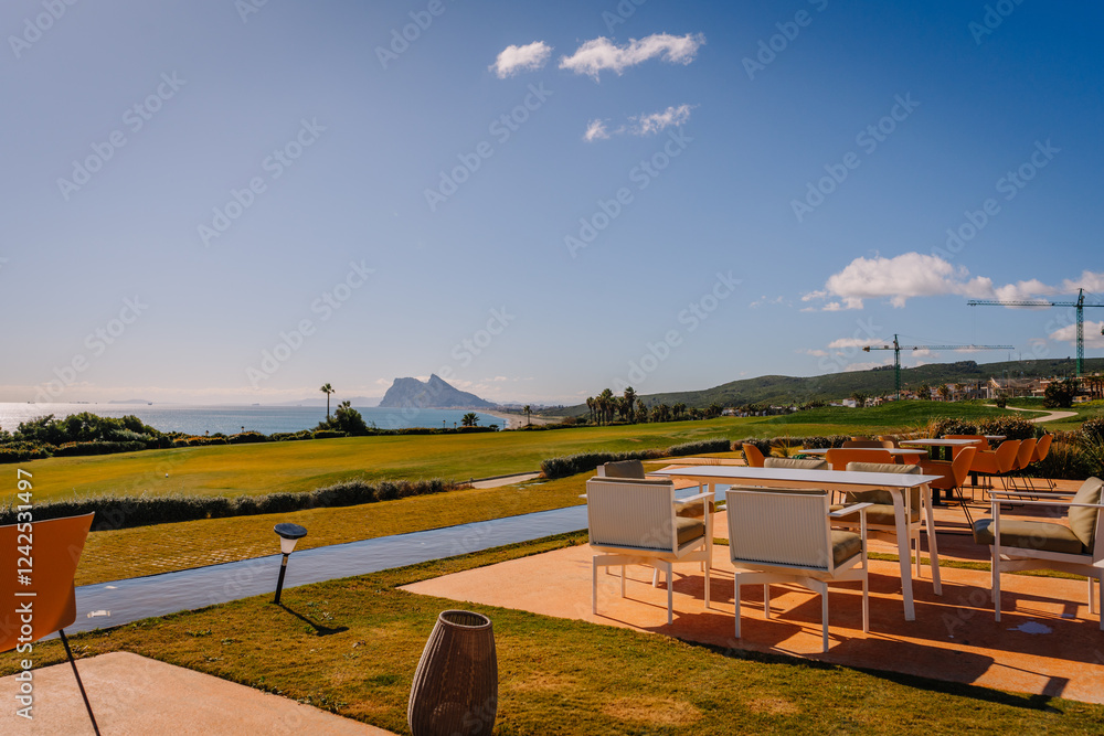Scenic patio with outdoor seating overlooking a golf course, ocean, and the iconic Rock of Gibraltar under a sunny blue sky. Scenic patio with outdoor seating overlooking a golf course, ocean, and the iconic Rock of Gibraltar under a sunny blue sky.