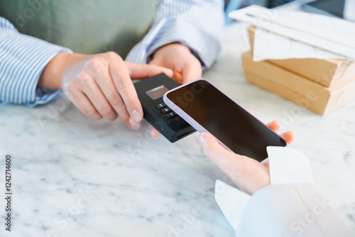 店舗で買う商品の支払いをスマートフォンのタッチ決済で行う女性の手元
