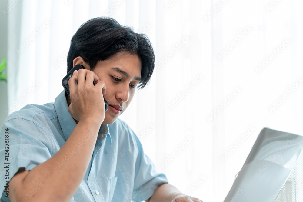 Asian young man use computer working from home and talking on the phone. Asian young man use computer working from home and talking on the phone.