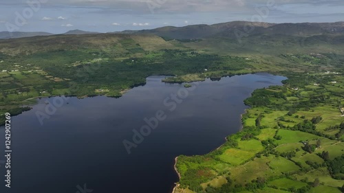 Lough Eske, County Donegal, Ireland, June 2023. Drone slowly pulls backwards, showcasing distant islets of the lake as sunlight warms grassy farmland, with rolling hills on the horizon. photo