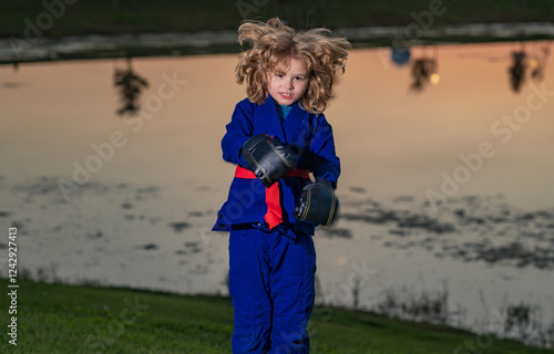 Kid boy in kimono practicing judo, taekwondo, jujitsu, kung-fu, jiu-jitsu, aikido outdoor. Sport karate kids. Little boy wearing kimono doing karate in park. Martial arts for kids. photo