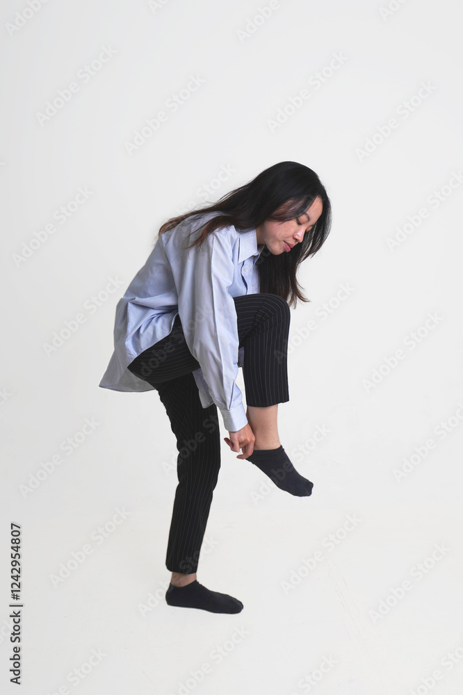 Young Indonesian woman with long hair wearing blue shirt and black pants putting on black socks isolated on vertical white background. Young Indonesian woman with long hair wearing blue shirt and black pants putting on black socks isolated on vertical white background.