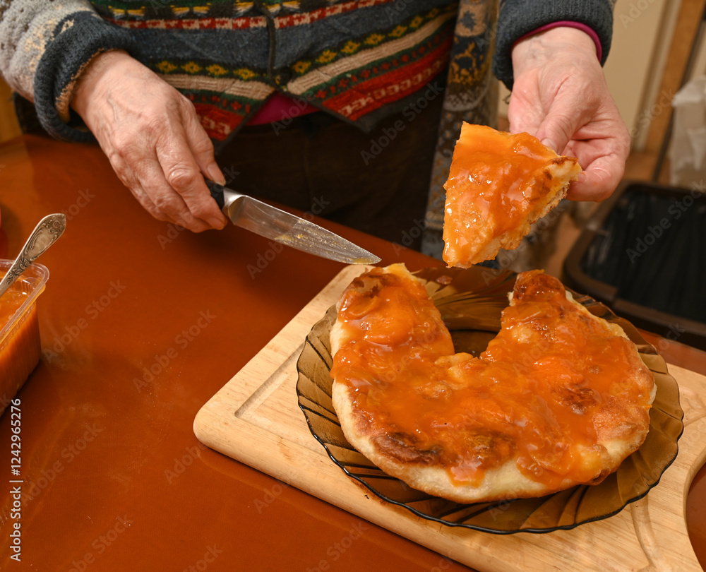Woman cutting a round, soft bread topped with apricot jam.