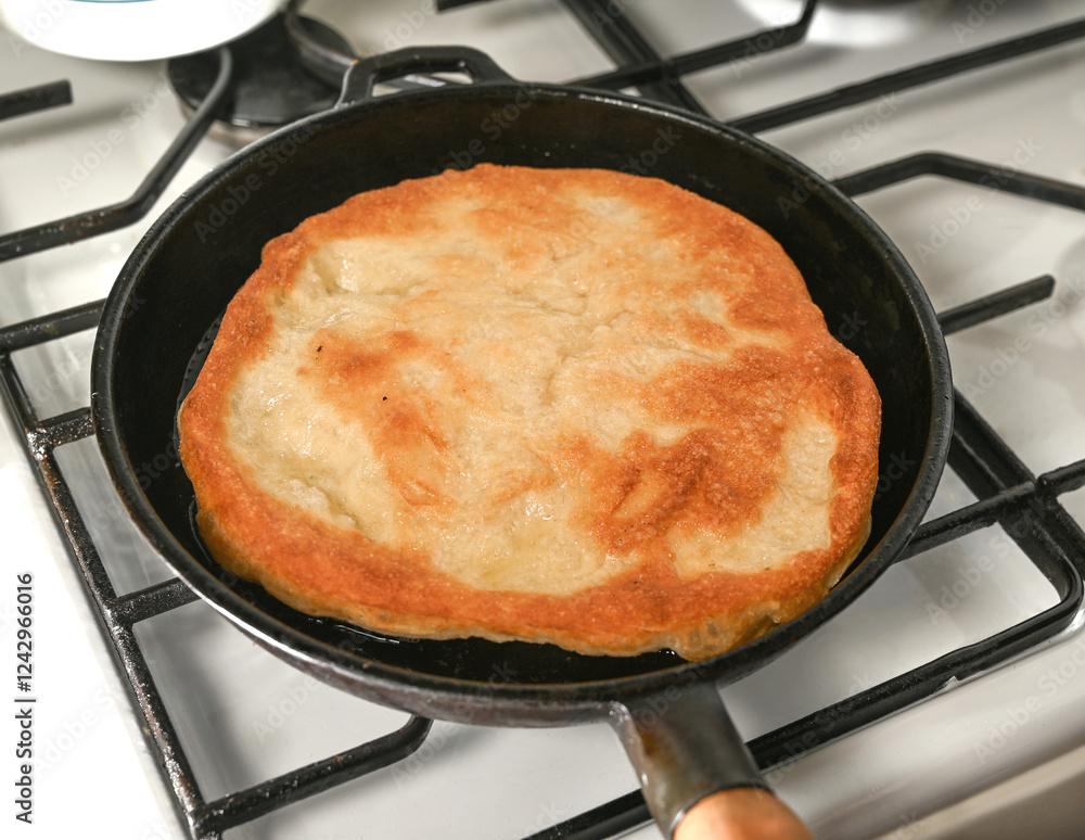 Golden flatbread cooking in a cast iron skillet on a gas stove during the afternoon