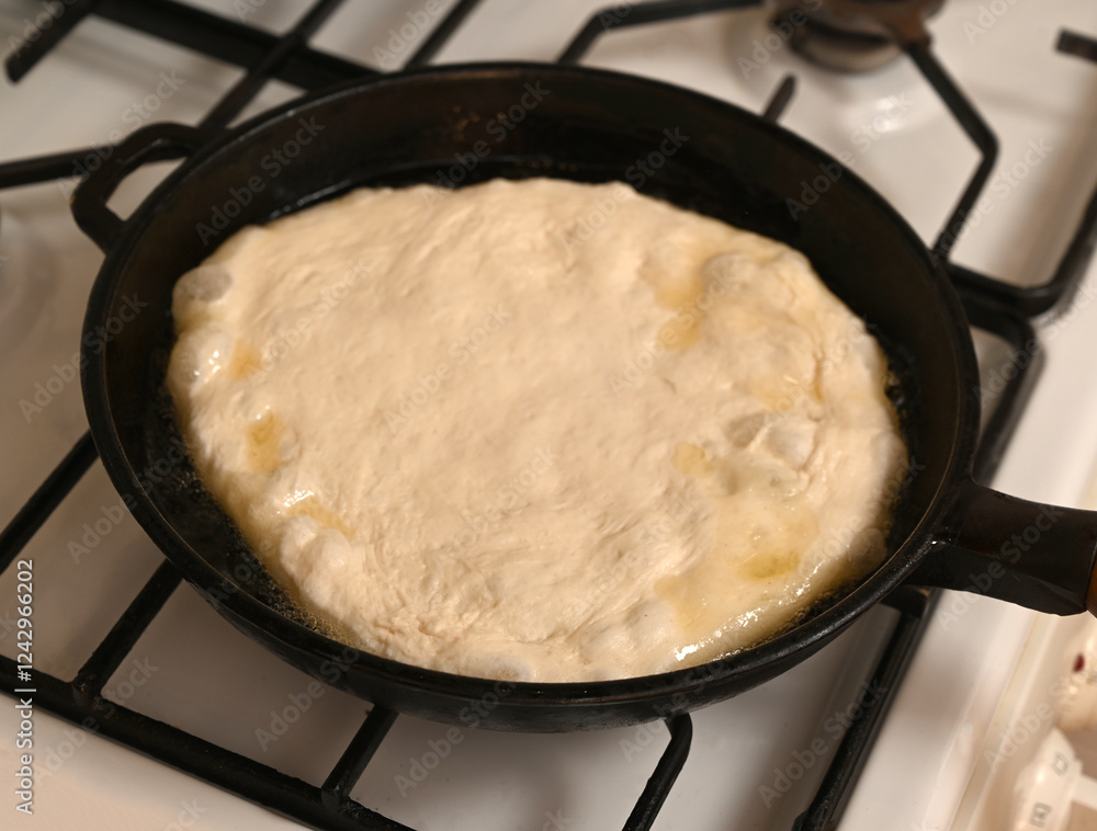 Dough rising in a cast iron skillet over a gas stove during meal preparation on a warm afternoon