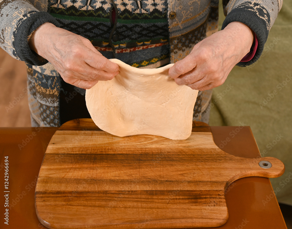 Hands skillfully stretching dough on a wooden board in a cozy kitchen setting during the afternoon