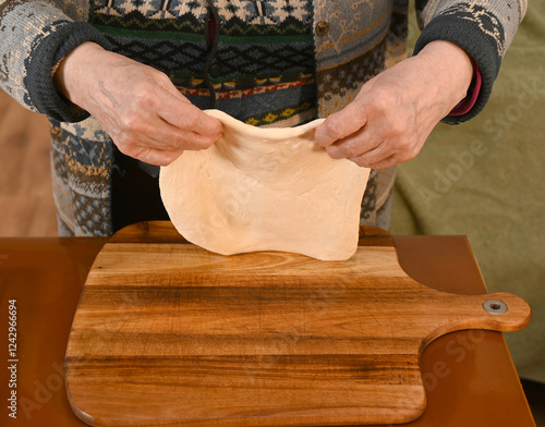 Obraz na płótnie Hands skillfully stretching dough on a wooden board in a cozy kitchen setting during the afternoon w salonie