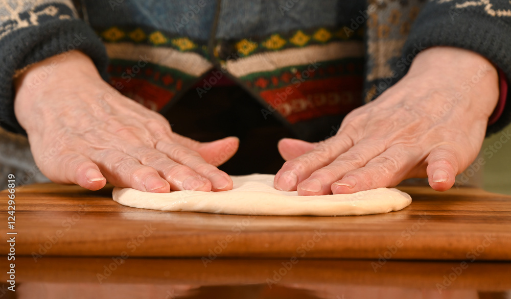 Woman preparing dough on a wooden surface in a cozy kitchen environment while wearing a warm sweater