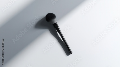 Close-up of a makeup brush on a white background. the brush has a black handle and a round, black bristled head. the bristles are densely packed and appear to be made of synthetic fibers. photo