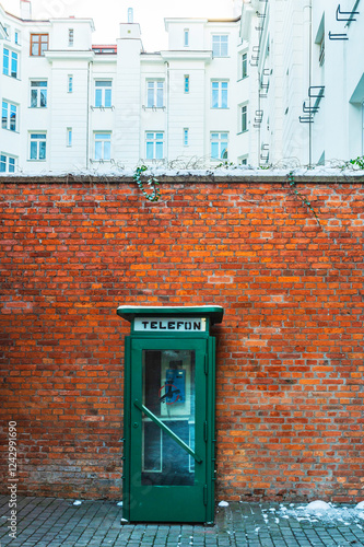 Stara zielona budka telefoniczna , na warszawskiej Pradze Północ stojąca przy murze z czerwonej cegły. photo