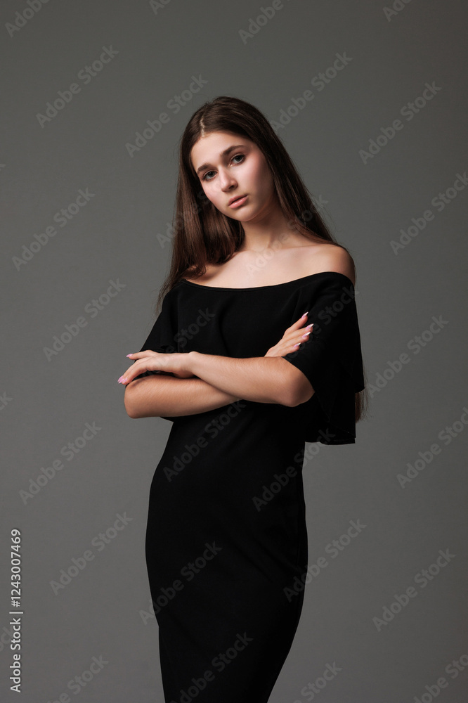 Young model poses elegantly in a black off-shoulder dress against a neutral background Young model poses elegantly in a black off-shoulder dress against a neutral background