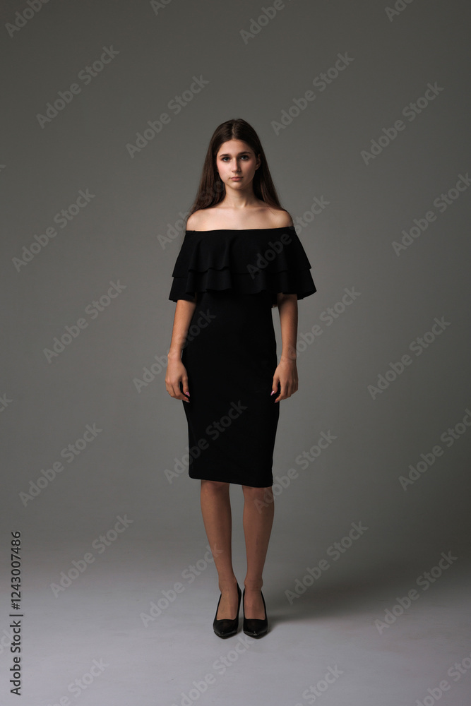 Female model poses elegantly in a stylish black off-the-shoulder dress against a neutral backdrop Female model poses elegantly in a stylish black off-the-shoulder dress against a neutral backdrop