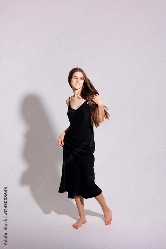 Young woman in a black dress poses elegantly against a plain background while showcasing long hair and natural beauty Young woman in a black dress poses elegantly against a plain background while showcasing long hair and natural beauty