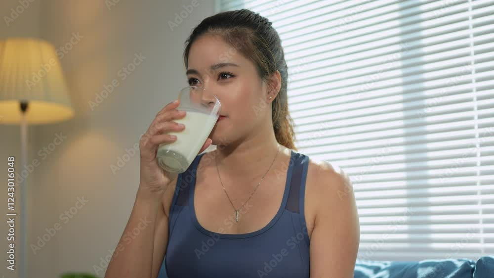 Sporty asian woman sitting comfortably on living room sofa, drinking fresh milk, embodying wellness through nutritious lifestyle and relaxed domestic moment Sporty asian woman sitting comfortably on living room sofa, drinking fresh milk, embodying wellness through nutritious lifestyle and relaxed domestic moment