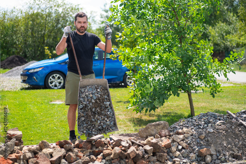 A man unload a wheelbarrow with crushed stone with blue car on background photo