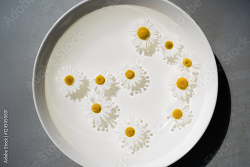 Obraz na płótnie Yellow flowers of chamomile slowly sway on a white plate on the surface of the water w salonie