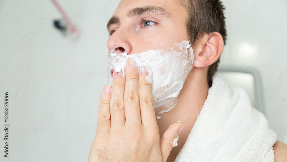 Young man applying shaving foam near mirror in bathroom Young man applying shaving foam near mirror in bathroom