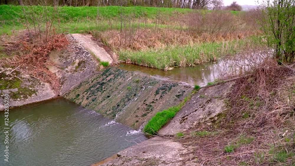 Water flows gently over a natural stone ledge in a serene river setting surrounded by lush greenery Water flows gently over a natural stone ledge in a serene river setting surrounded by lush greenery