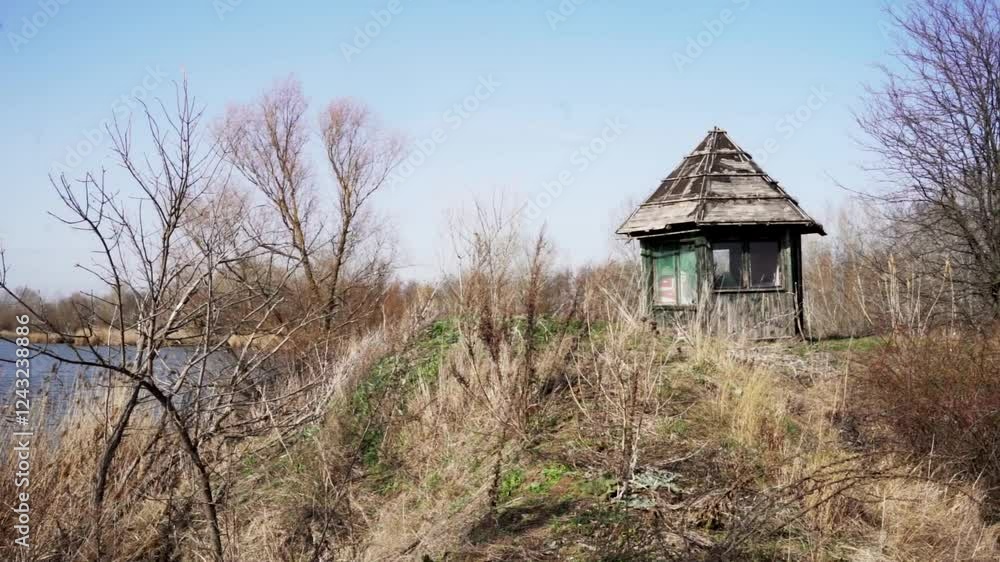 Scenic riverside view with a rustic shelter amidst barren trees and grassland in early spring Scenic riverside view with a rustic shelter amidst barren trees and grassland in early spring