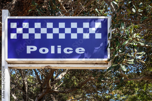 Blue and white checkered pattern Western Australia police force sign, board. Rottnest Island, tourism, travel destination hot spot. Branches of Moreton Bay fig tree (Ficus macrophylla) photo