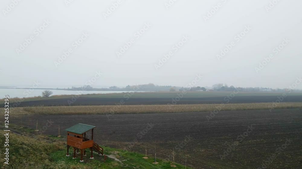 Fields under a cloudy sky with distant trees and a small structure in the foreground Fields under a cloudy sky with distant trees and a small structure in the foreground