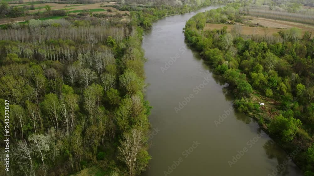 River flows through lush greenery in serene landscape at sunrise near small rural settlement River flows through lush greenery in serene landscape at sunrise near small rural settlement