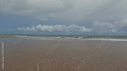 Beach waves sliding over a sandbank during a cloudy and stormy day. Winter vacation landscape