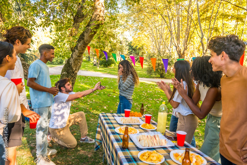 Man proposing marriage to woman during picnic with friends photo