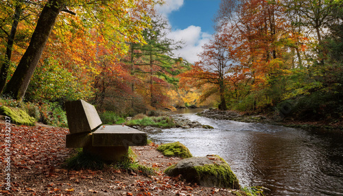 A concrete bench overlooks a peaceful river surrounded by trees displaying vibrant autumn foliage in orange and green hues. photo