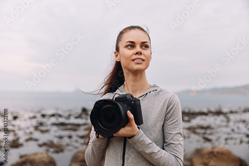 Young woman with a camera on the beach, showcasing creativity and confidence in photography, wearing casual grey sportswear, with an ocean background in soft natural colors photo