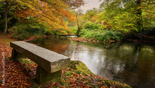 A concrete bench overlooks a peaceful river surrounded by trees displaying vibrant autumn foliage in orange and green hues. photo