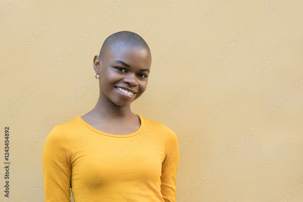 Obraz premium Smiling African woman with a shaved head in a vibrant yellow sweater