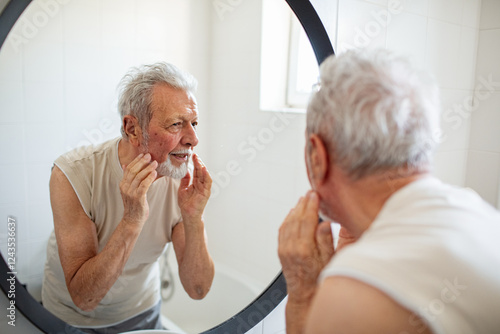 Senior man grooming his beard in front of bathroom mirror photo