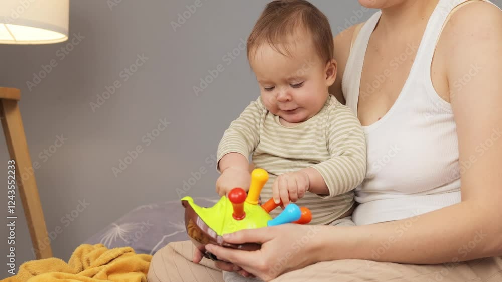 A young child engages with a bright, interactive toy while seated on a soft surface. The caregiver supports the child, fostering exploration and learning in a warm, inviting atmosphere A young child engages with a bright, interactive toy while seated on a soft surface. The caregiver supports the child, fostering exploration and learning in a warm, inviting atmosphere