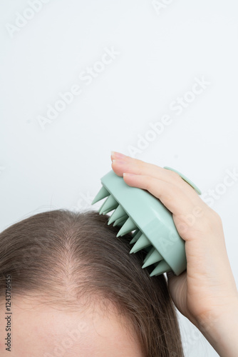 Woman using a scalp massager to stimulate hair growth and care for scalp, vertical, copy space. Concept of beauty treatment, wellness, and addressing alopecia and thinning hair through daily routines.