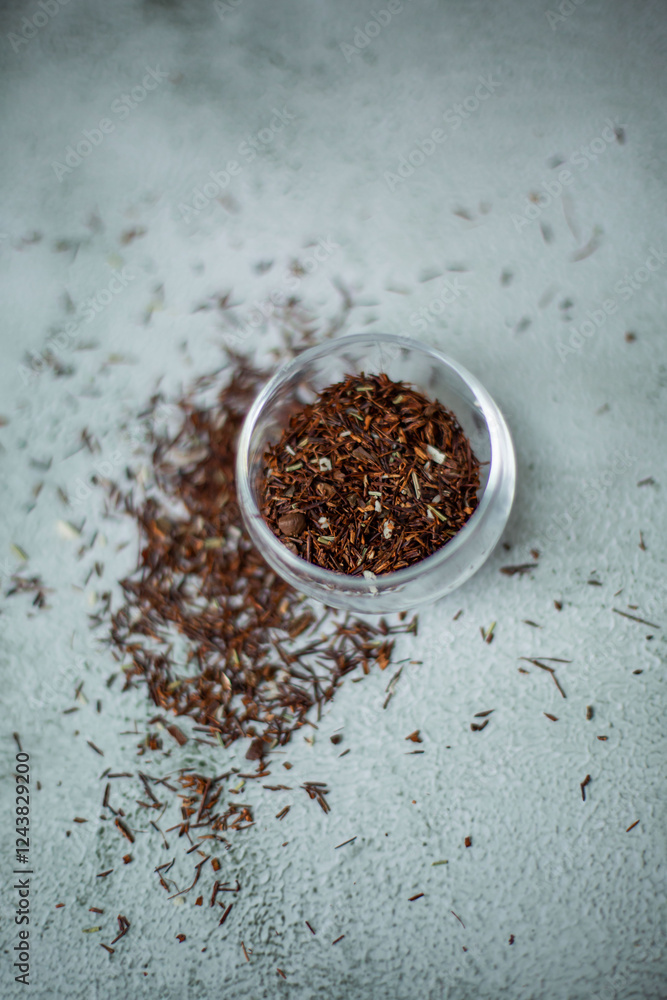 A tea cup on a table with a teapot and scattered tea leaves A tea cup on a table with a teapot and scattered tea leaves