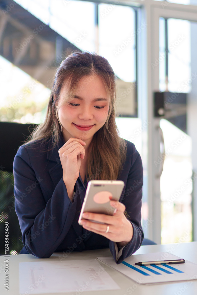 Close-up of a young Asian businesswoman using a smartphone while working in a bright and modern office Close-up of a young Asian businesswoman using a smartphone while working in a bright and modern office