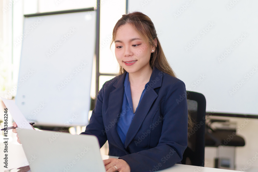 Young Asian businesswoman working on a laptop in a modern office, wearing a professional suit Young Asian businesswoman working on a laptop in a modern office, wearing a professional suit