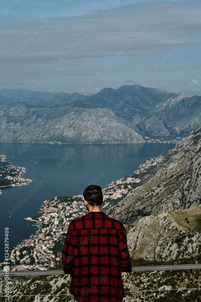 A young Caucasian man in a red plaid shirt stands on an observation deck overlooking the Bay of Kotor. Rear view. The southernmost fjord in the Adriatic Sea, Montenegro. Travel concept A young Caucasian man in a red plaid shirt stands on an observation deck overlooking the Bay of Kotor. Rear view. The southernmost fjord in the Adriatic Sea, Montenegro. Travel concept