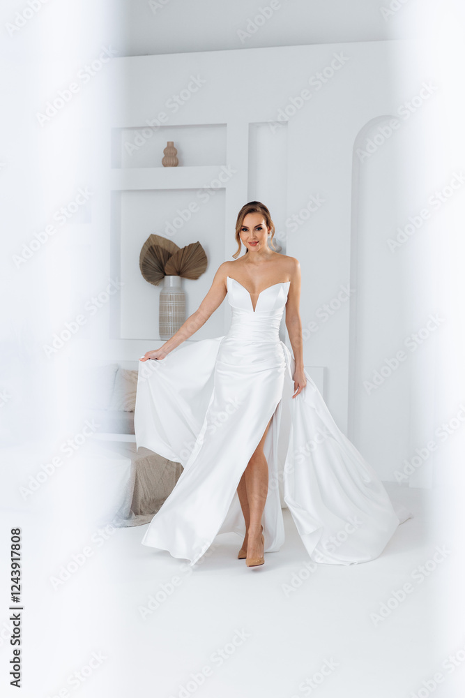 Fototapeta premium Bride in a dress with a train that flutters around on a white background. Stylish trendy wedding 2025
